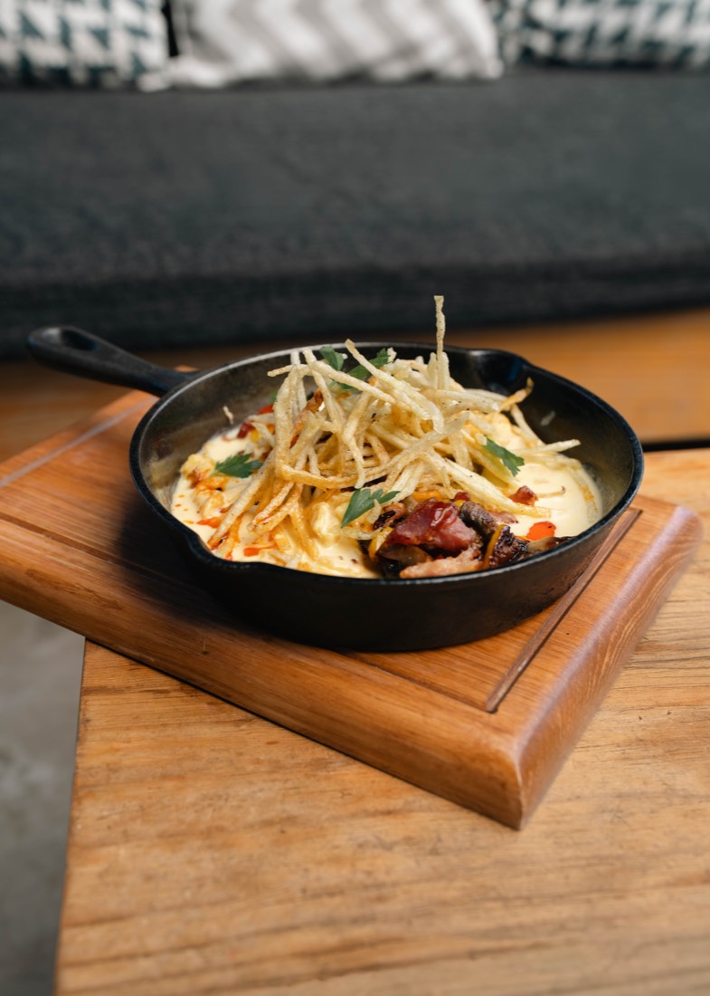 Cazuela de barro con huevo, papa y queso gratinado sobre tabla de madera