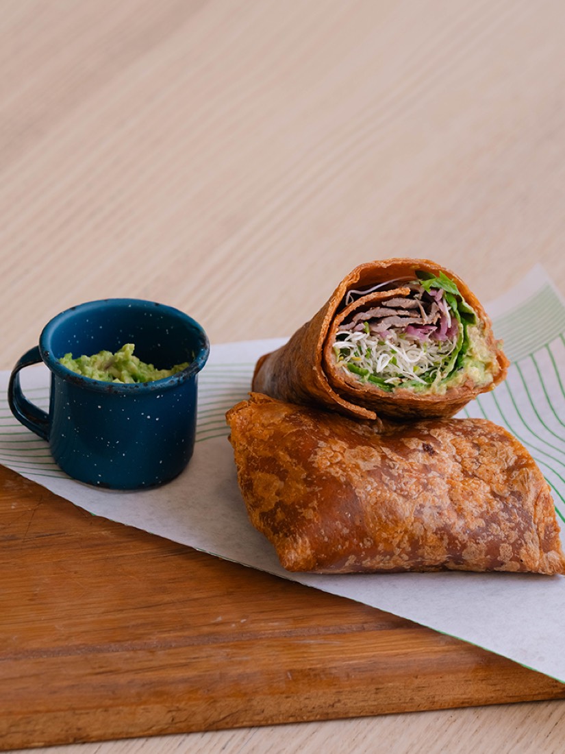 Wrap de cecina partido a la mitad, con guacamole en taza azul