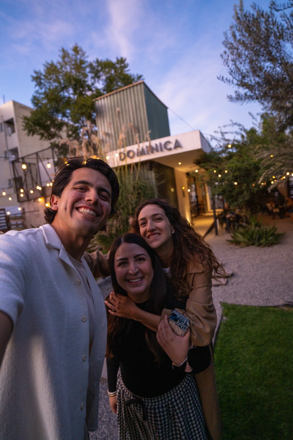 Tres amigos posando frente a la fachada de Dominica 19 al atardecer